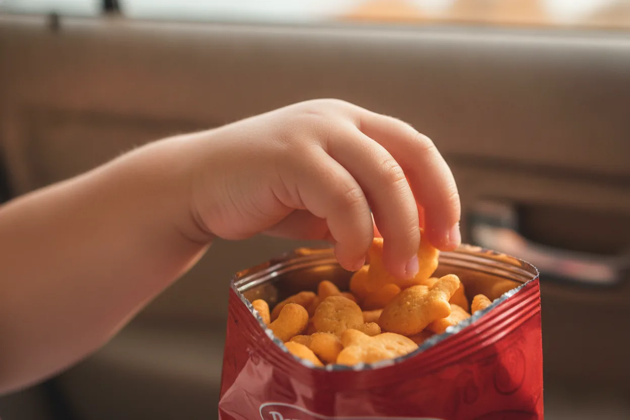 Close-up of a child's hand reaching into a bag of Goldfish crackers inside a car.