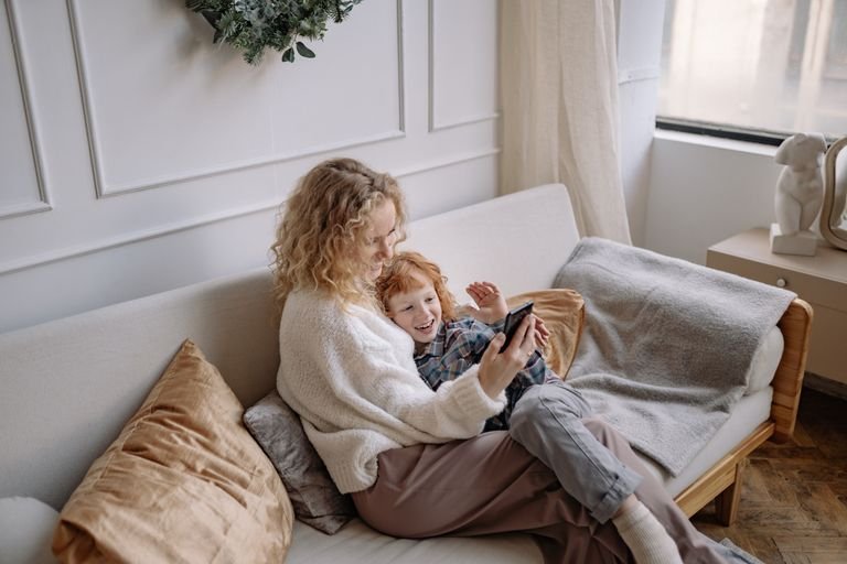 Happy mother and son taking a selfie on a cozy sofa indoors.