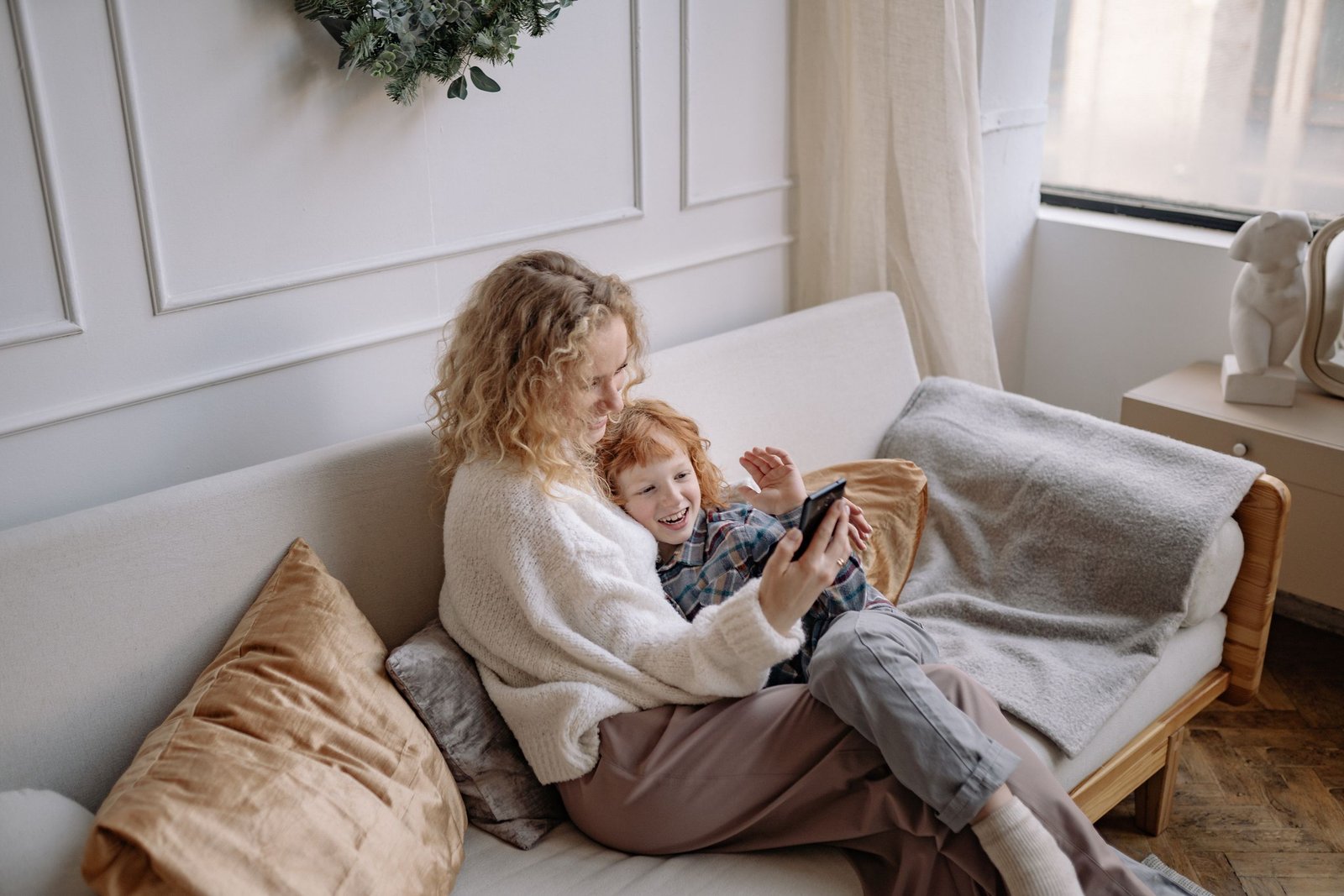 Happy mother and son taking a selfie on a cozy sofa indoors.