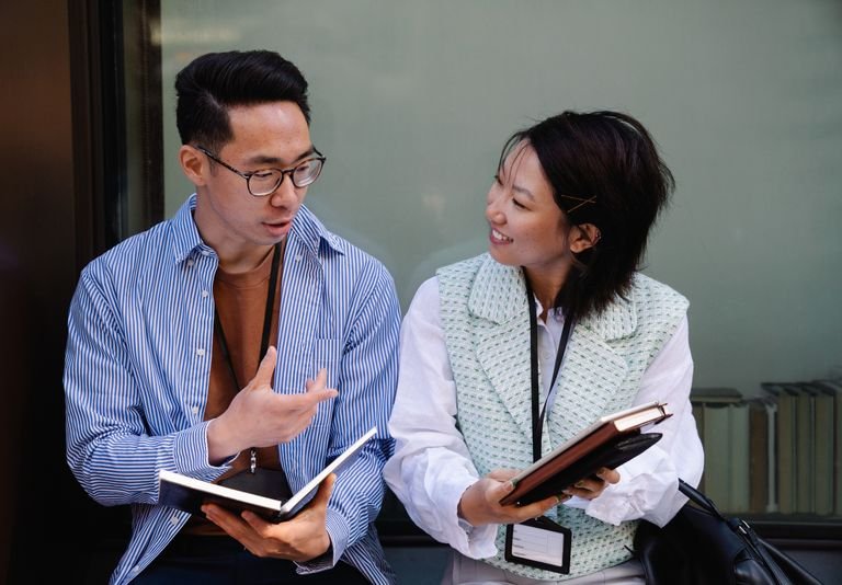 Two adults engaging in a conversation, holding notebooks, fostering teamwork and collaboration.