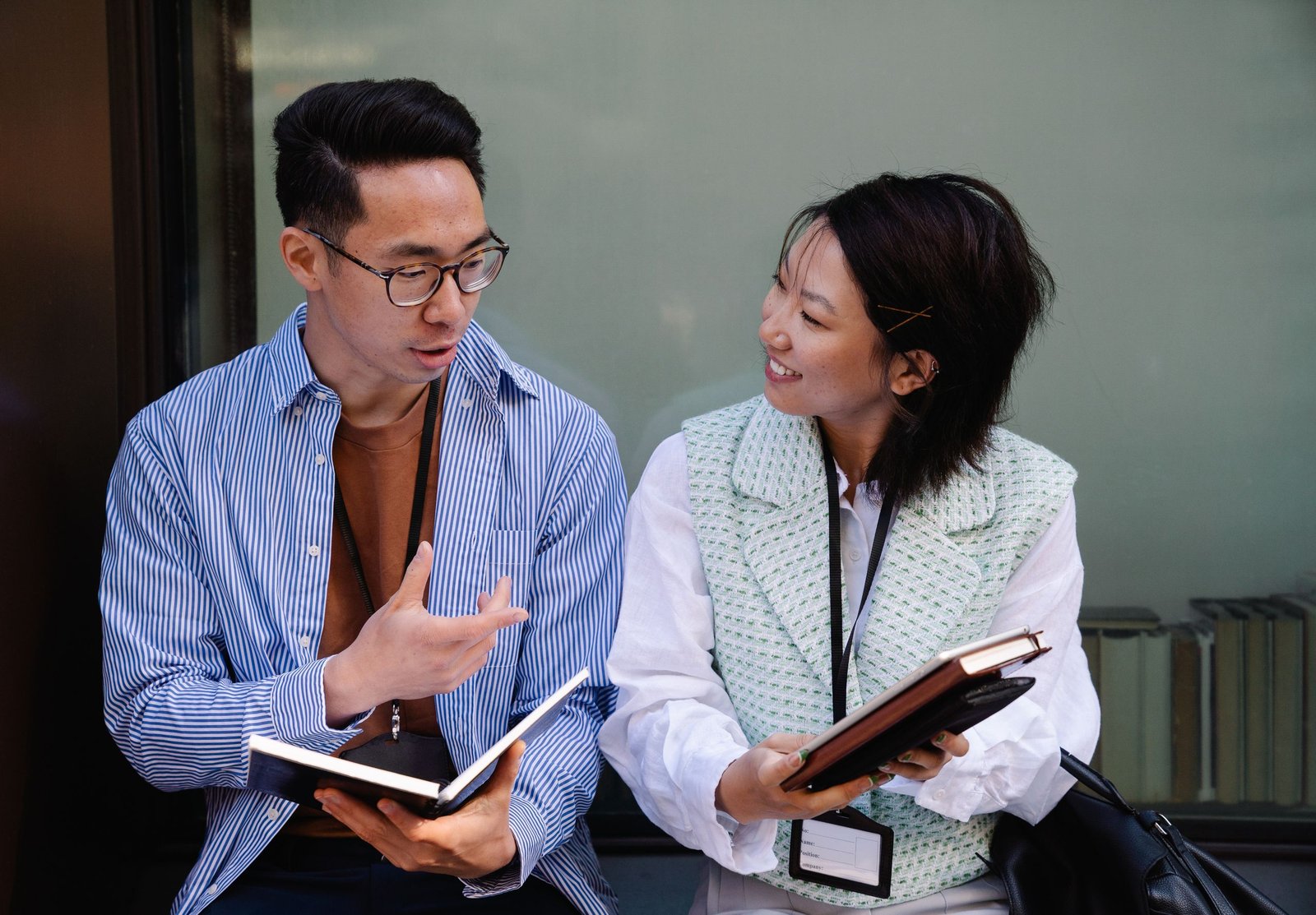 Two adults engaging in a conversation, holding notebooks, fostering teamwork and collaboration.